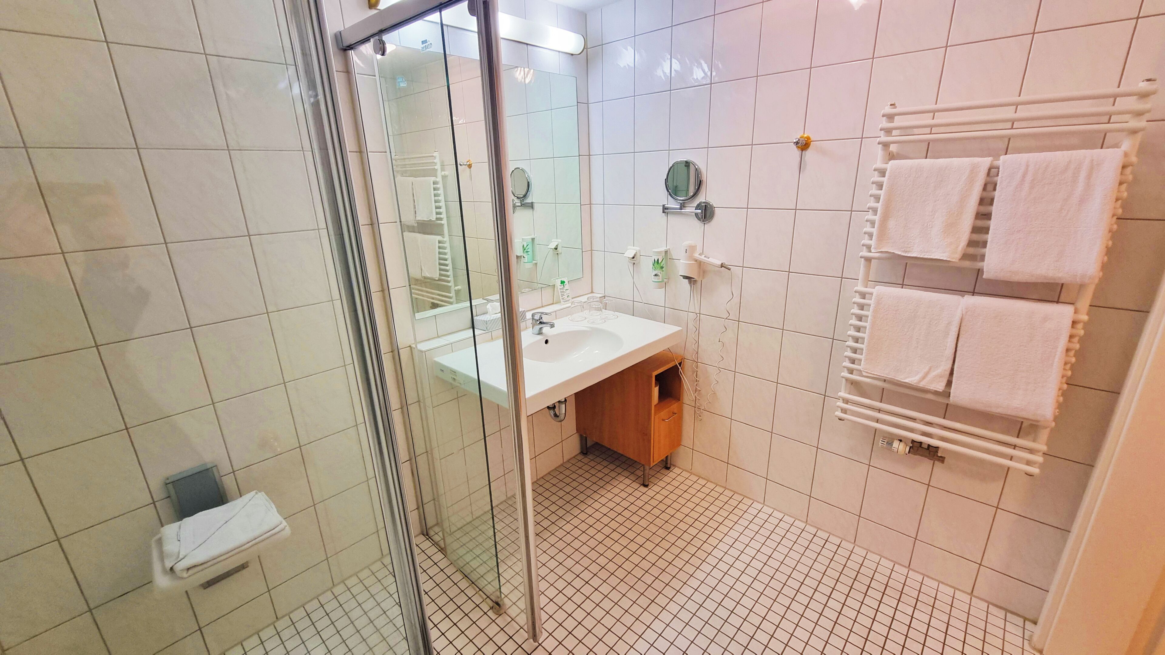 A bathroom with a glass shower enclosure, a sink with a mirror, and a towel rack with multiple towels.