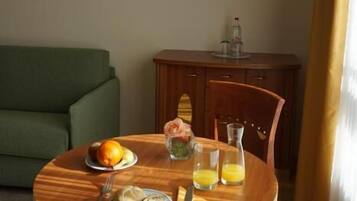 A dining area with a round wooden table, a green sofa, and a painting of a cityscape on the wall.