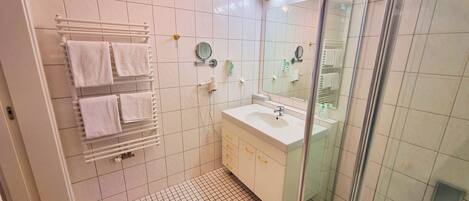 A modern bathroom with a glass shower enclosure, a white sink, and a towel rack with multiple towels.