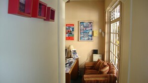Un pasillo estrecho con un escritorio, un sofá a rayas y un cartel en la pared.