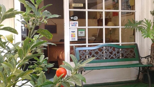 Entrada de un edificio con un banco verde, un cartel que indica acceso a WiFi y un letrero que dice 'ABIERTO'.