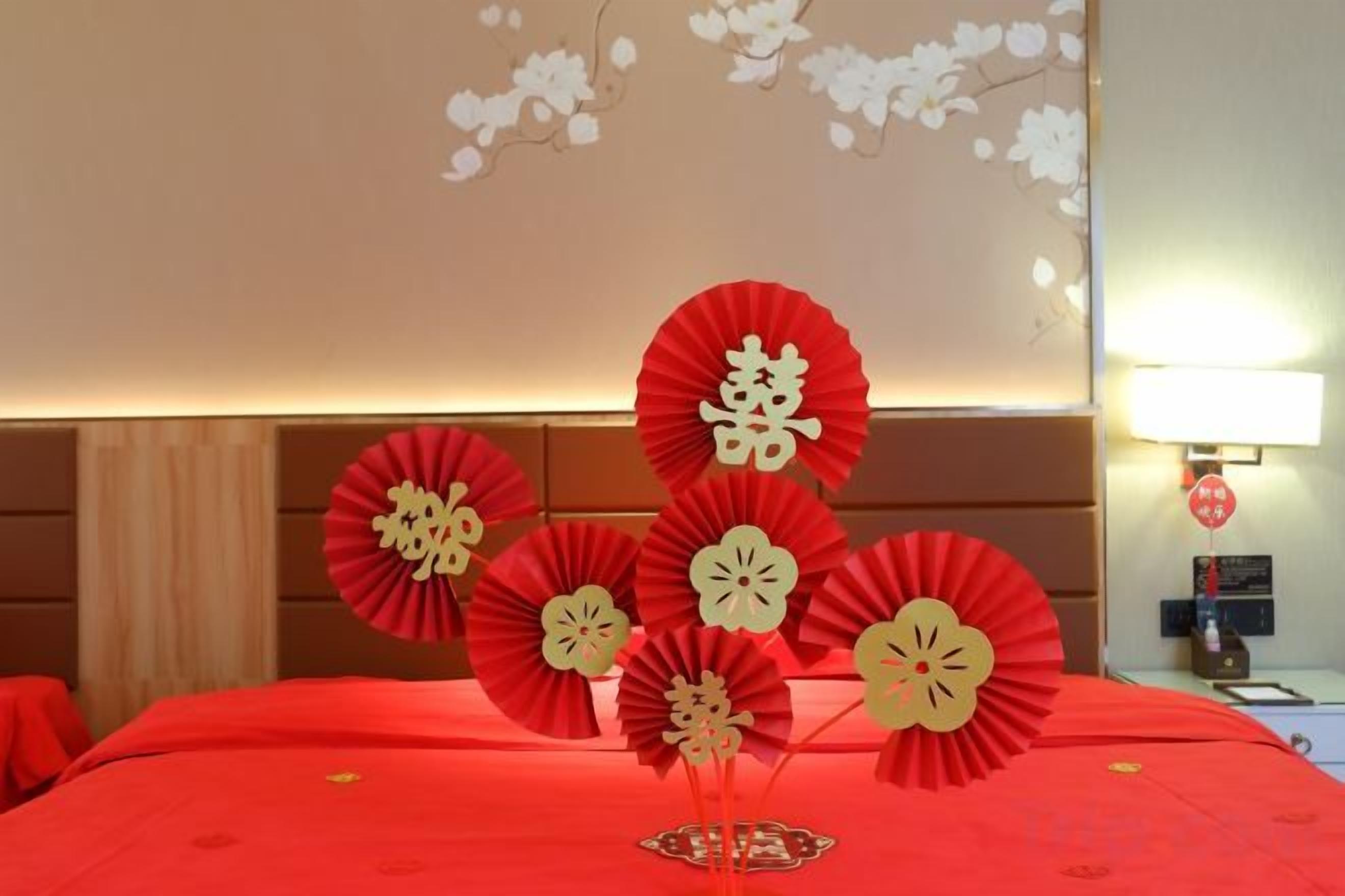 Una habitación de hotel con una colcha roja, abanicos decorativos de papel y una pared con diseño floral.