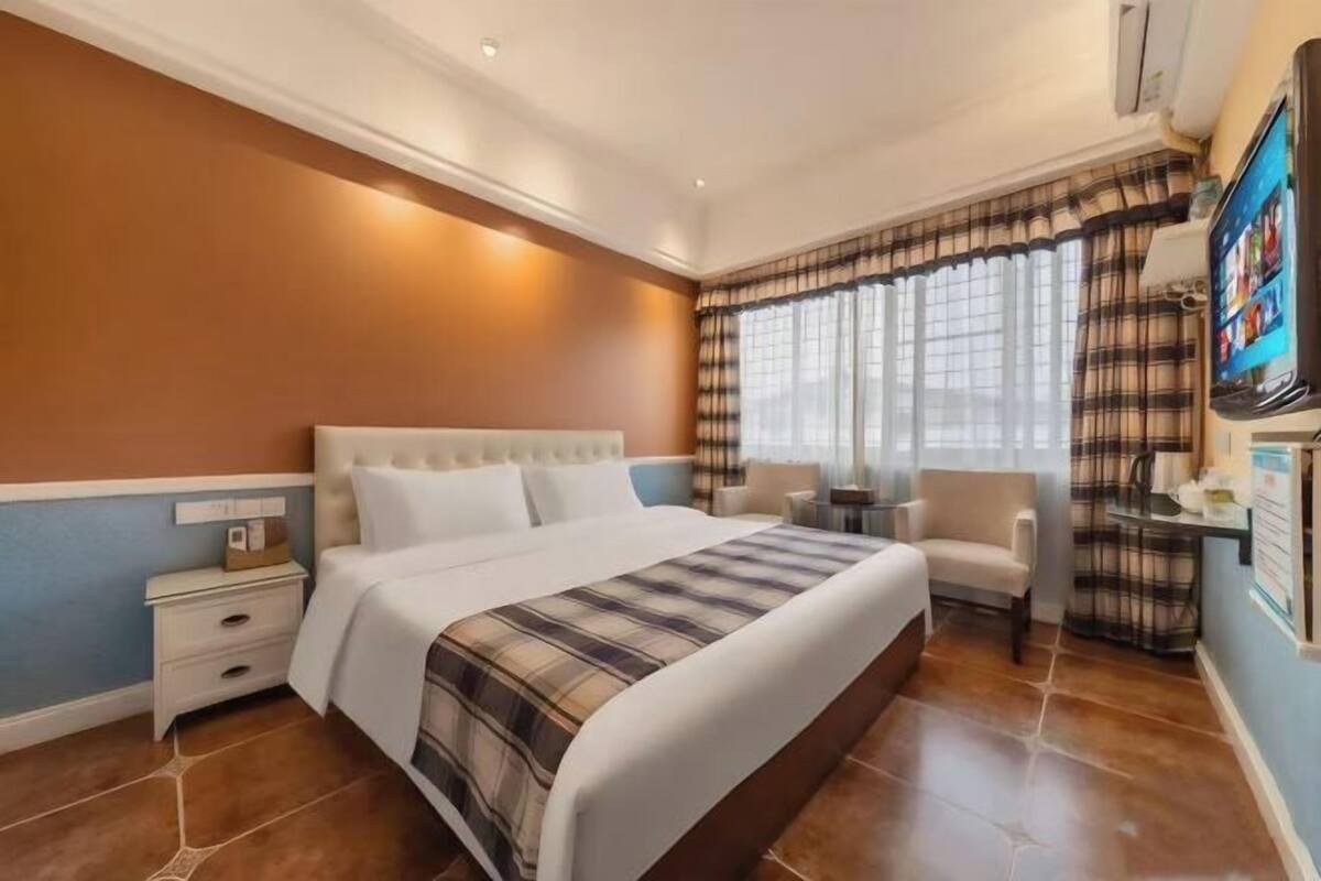 A hotel room with a large bed, a bedside table, a chair, a small table, and a TV.