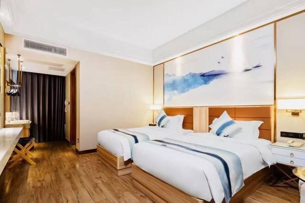 A hotel room with two beds, a desk, and a painting on the wall.