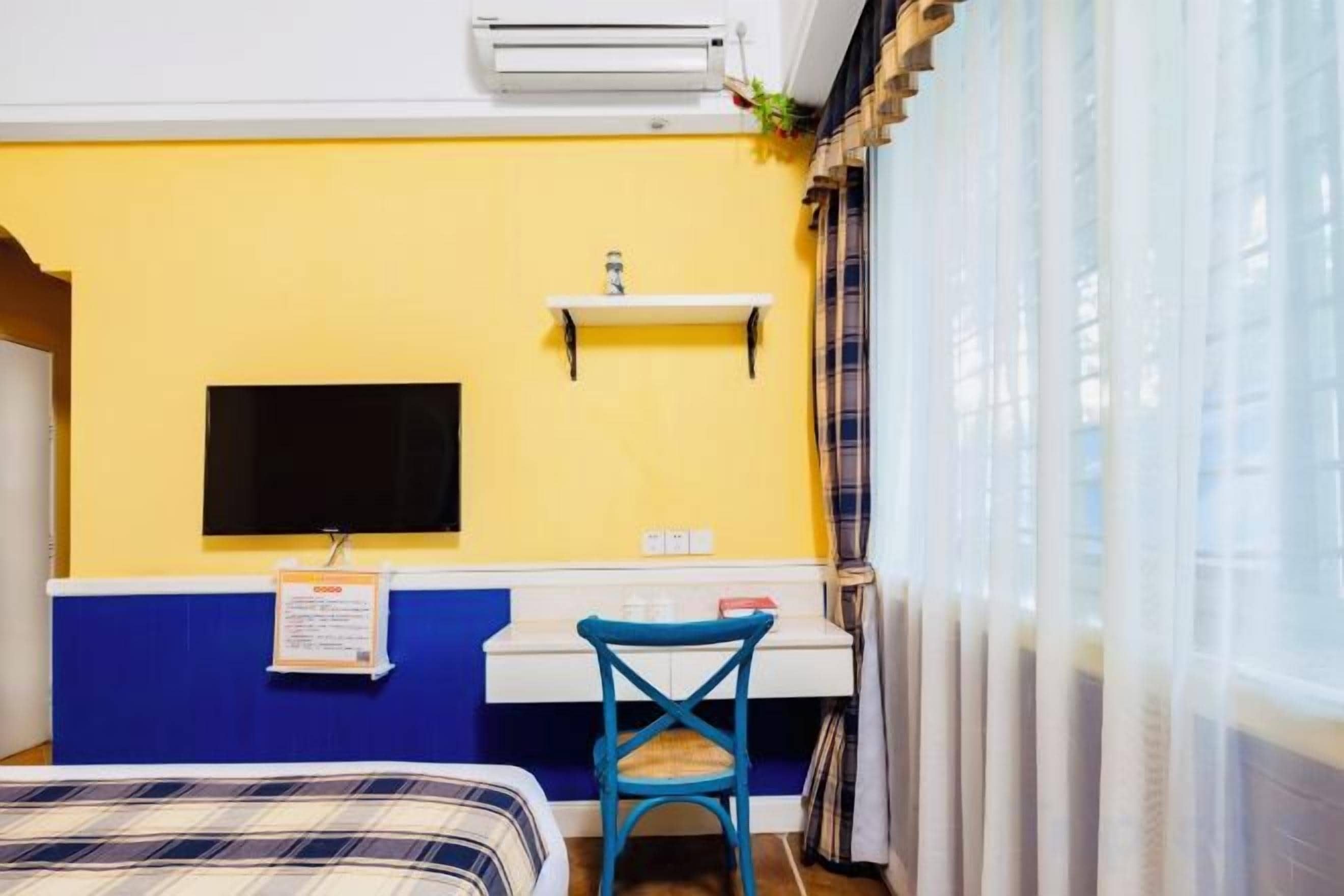 Une chambre d’hôtel équipée d’un lit, d’un bureau, d’une chaise, d’un téléviseur fixé au mur et d’une fenêtre avec des rideaux.