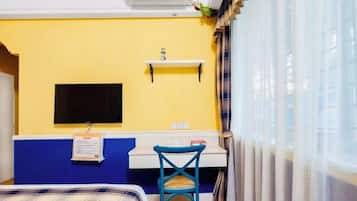 Une chambre d’hôtel équipée d’un lit, d’un bureau, d’une chaise, d’un téléviseur fixé au mur et d’une fenêtre avec des rideaux.