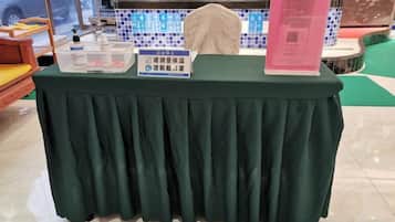 Una mesa con mantel verde, un cartel, un código QR y un recipiente de plástico.
