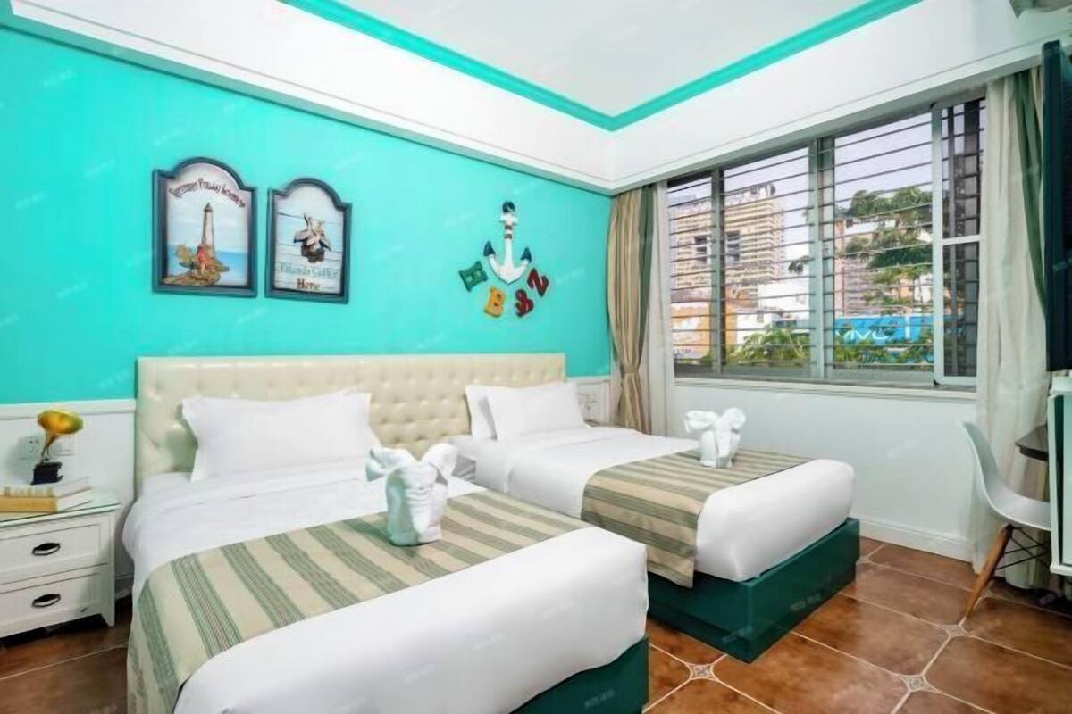 A hotel room with two beds, a window with curtains, and a view of buildings outside.