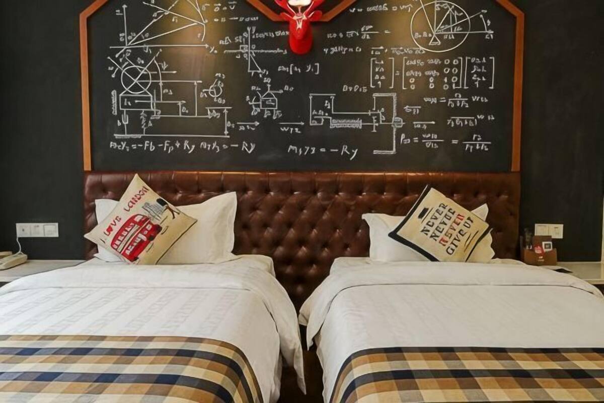 A hotel room with a bed, two pillows, a headboard, and a wall with mathematical equations.