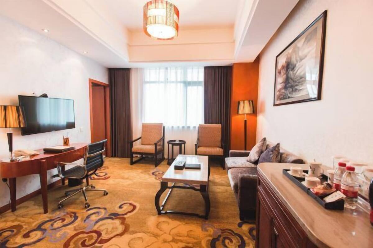 Habitación de hotel con televisión, escritorio, sofá, mesa de centro y zona de comedor.