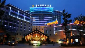 A multi-story hotel with a prominent sign at the top, a well-lit entrance, and a courtyard area.