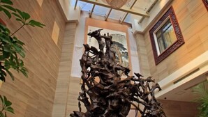 A lobby with a large abstract sculpture, wooden paneling, a large window with a decorative frame, and a hanging light fixture. - Cangxi International Hotel (Cangxi)