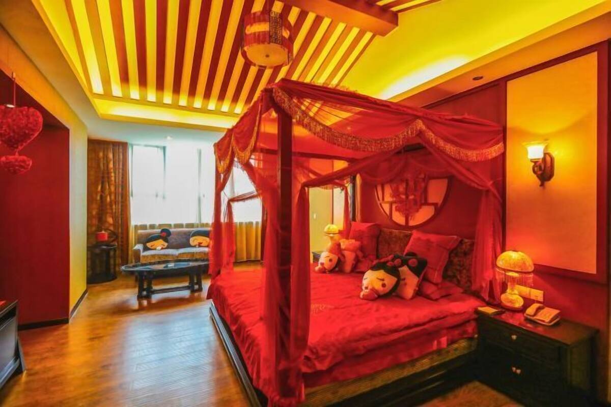 Una habitación con cama con dosel rojo, un sofá, una mesita y una lámpara.