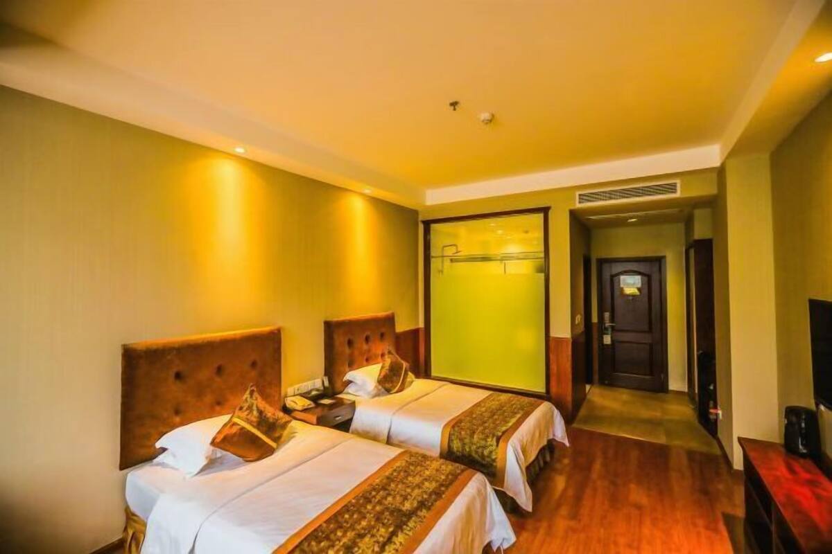 Habitación de hotel con dos camas, un televisor y una puerta que da a un pasillo.