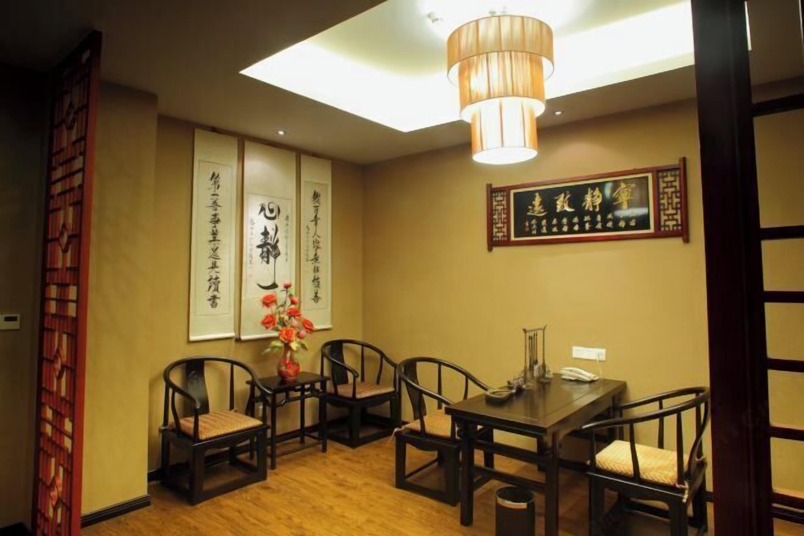 A traditional dining room with a wooden table and chairs, a hanging light fixture, and calligraphy on the walls.