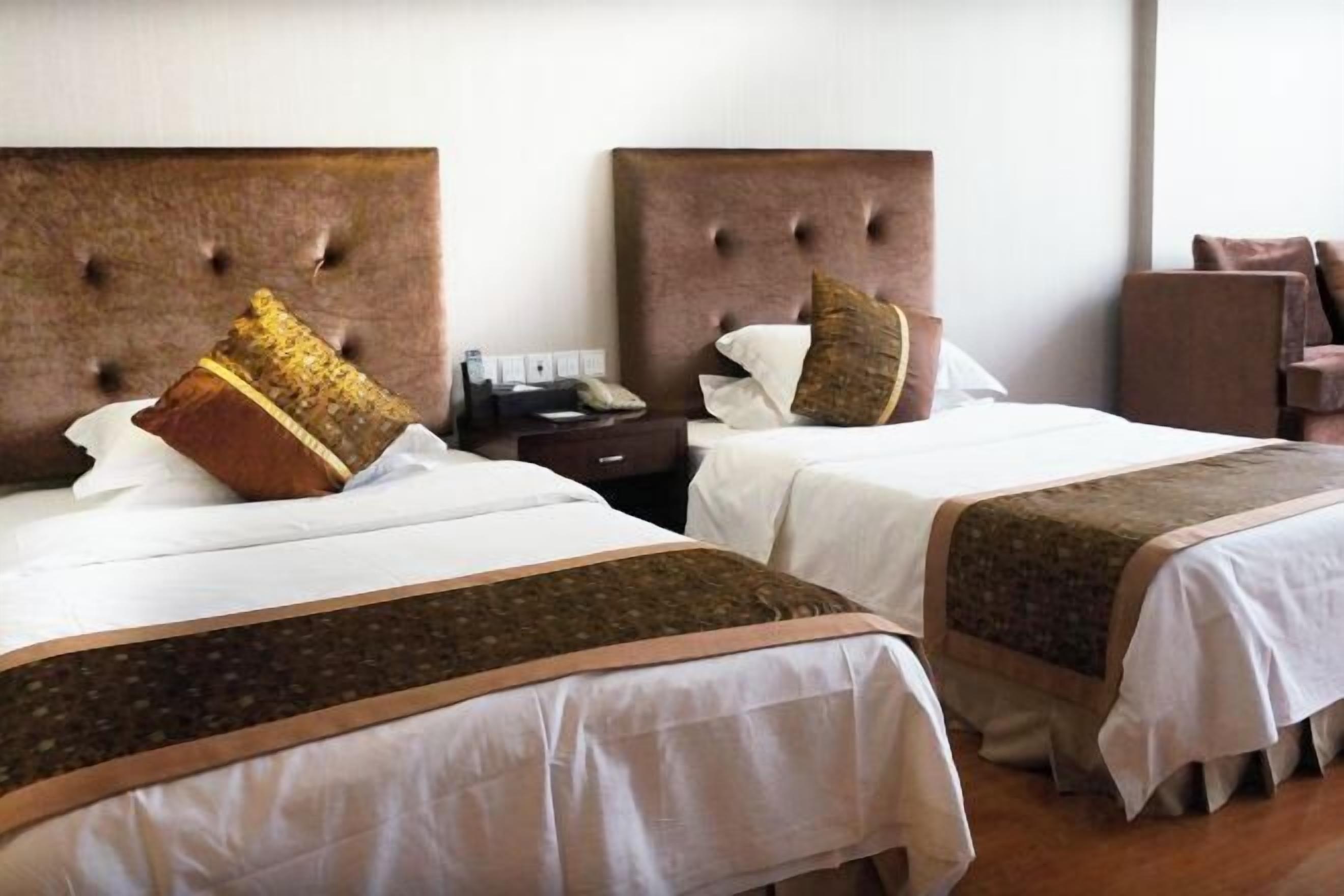Dos camas con cabeceros capitonados, una mesita de noche con teléfono y una silla en una habitación de hotel.