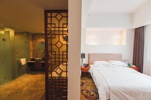 Habitación de hotel con cama, mesita de noche, escritorio y baño con lavabo y espejo.