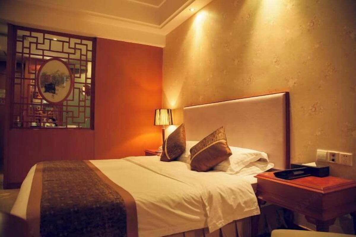 Habitación de hotel con cama, mesita de noche, lámpara y un biombo decorativo.