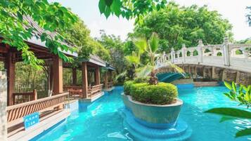 A serene indoor pool area with a bridge, surrounded by lush greenery and traditional architecture.