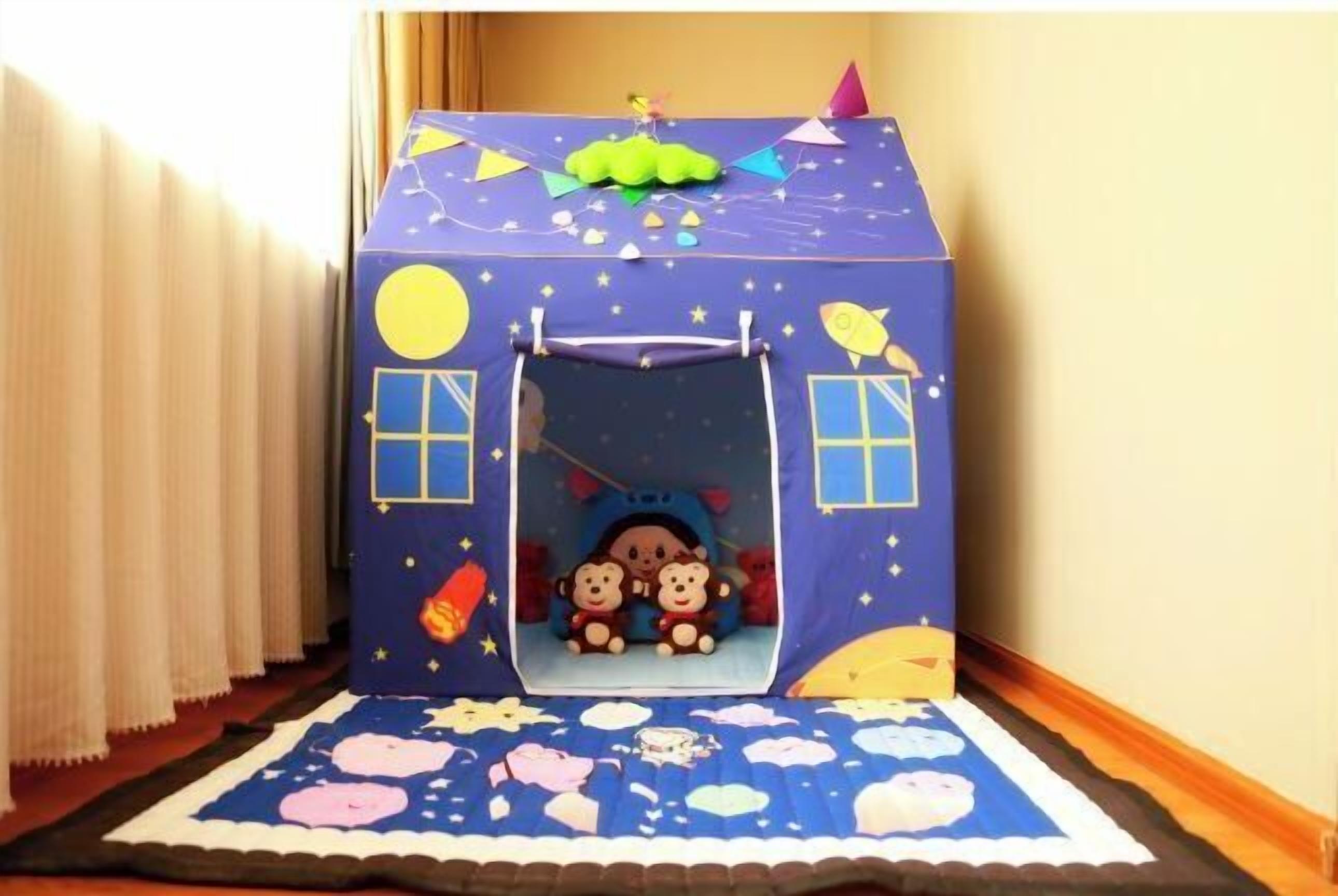 Una casita de juegos con un tobogán, dos osos de peluche en su interior y un tema de noche estrellada.