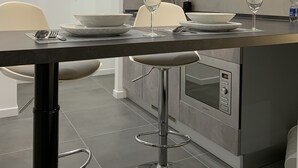 A modern kitchen with a dining area, including a bar stool, a dining table with plates and glasses, and a built-in oven. - ApartHotel Bossi (Milan)
