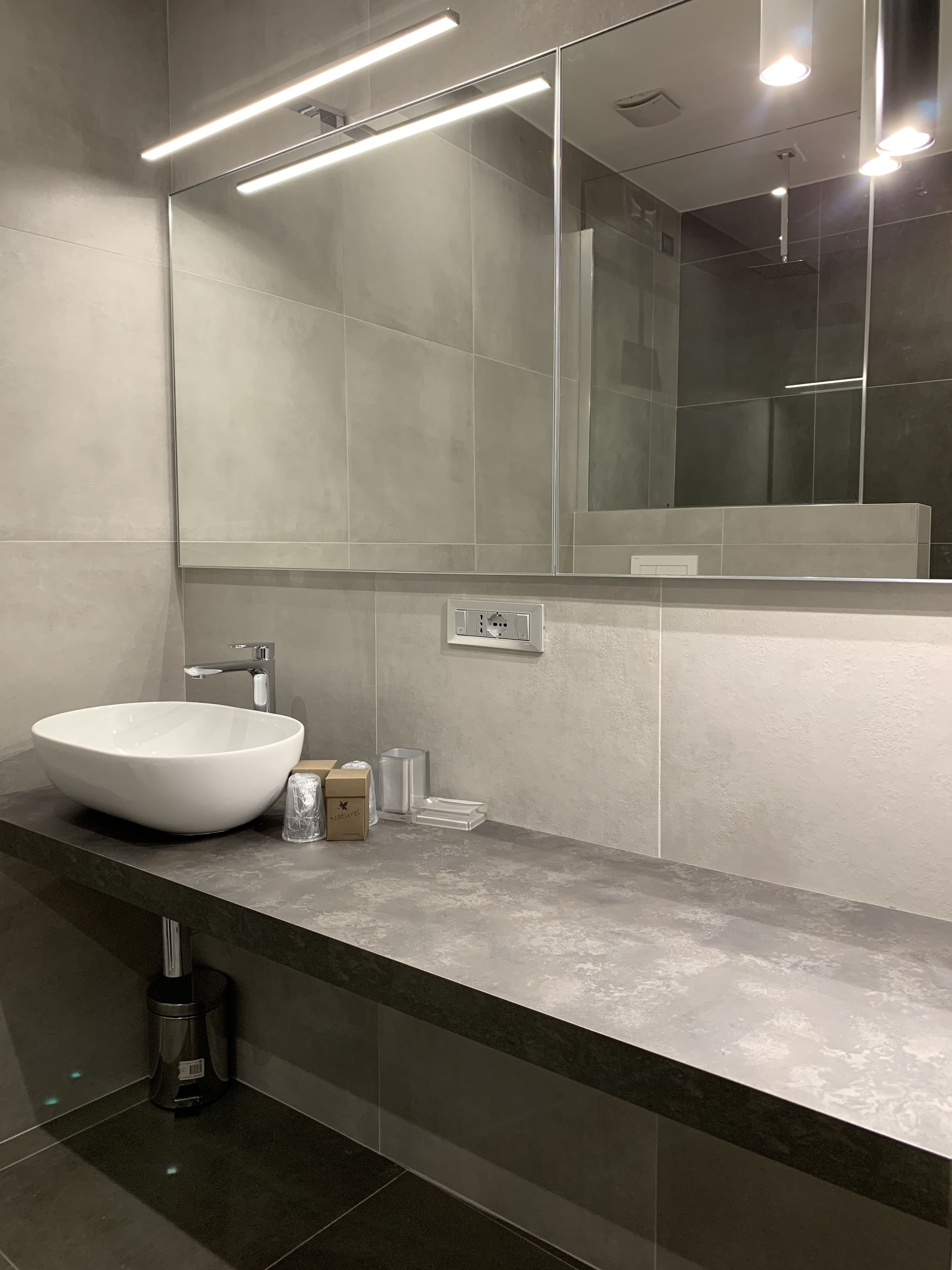 A modern bathroom with a large mirror, a white vessel sink, and a sleek countertop.