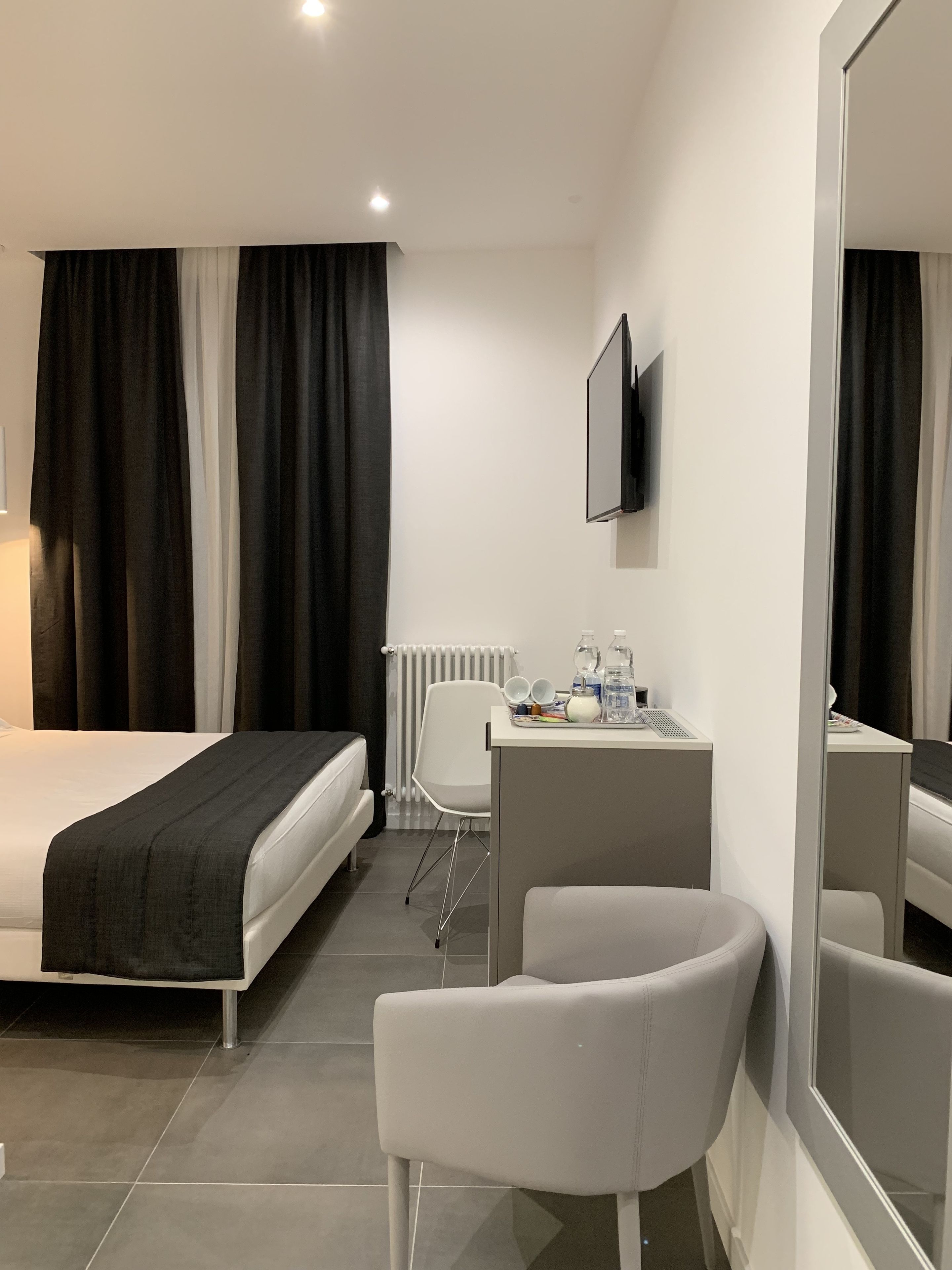 A hotel room with a bed, a desk, a chair, a mirror, and a TV.