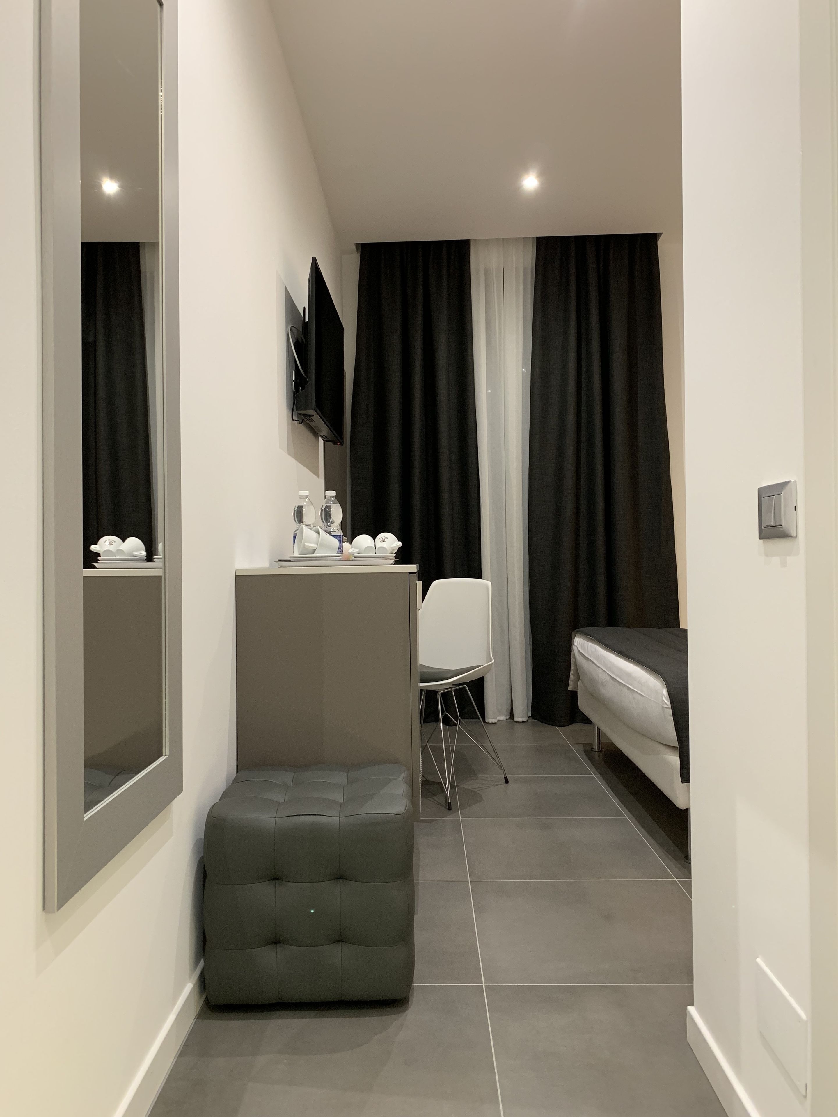 Una habitación de hotel moderna con una cama, un pequeño escritorio con una silla, un sofá y un espejo grande.