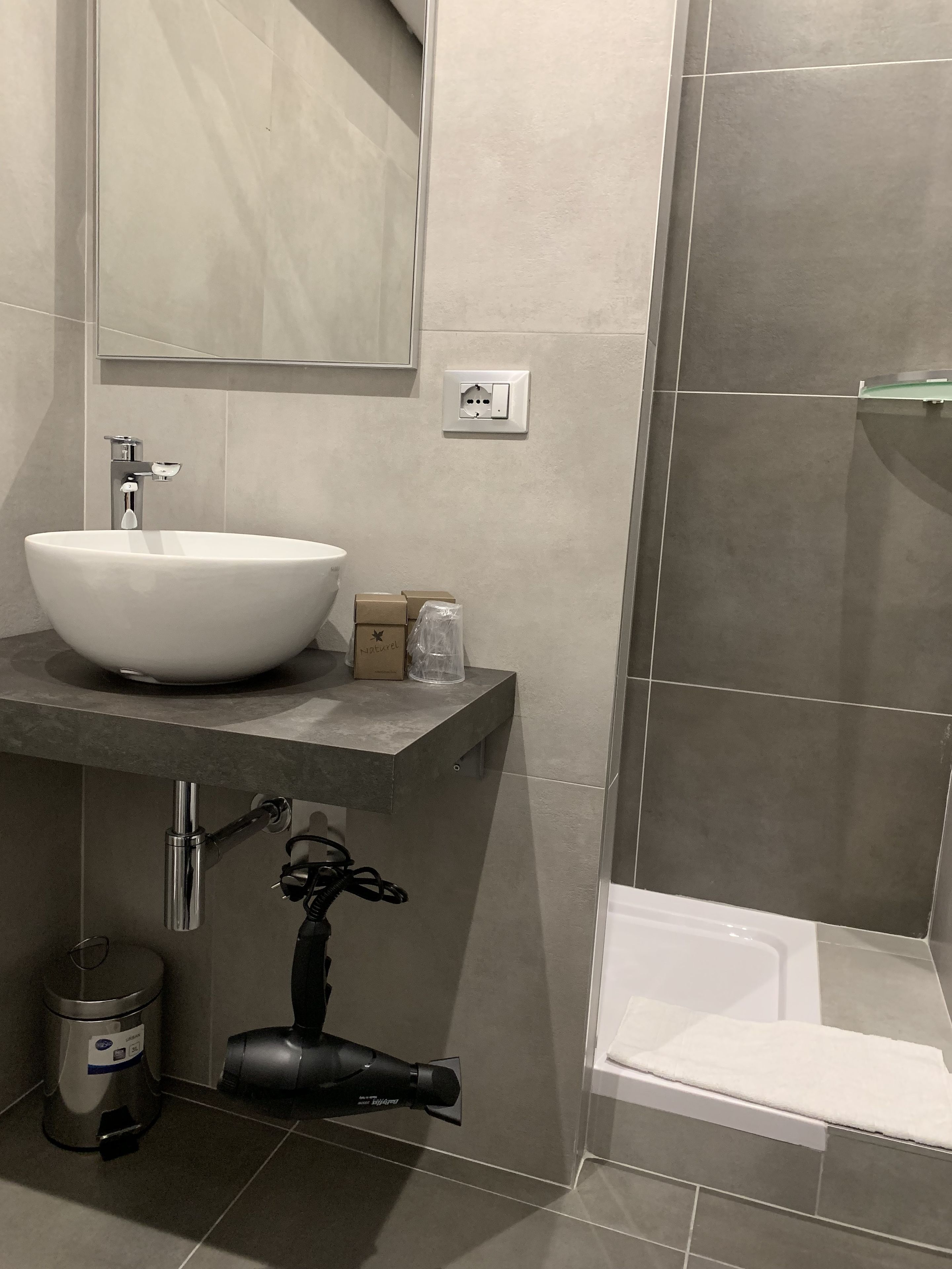 A modern bathroom with a large white sink, a mirror, and a shower area.