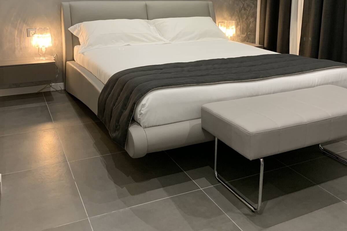 Un dormitorio moderno con una cama grande, lámparas de noche, un banco y una pared con textura.