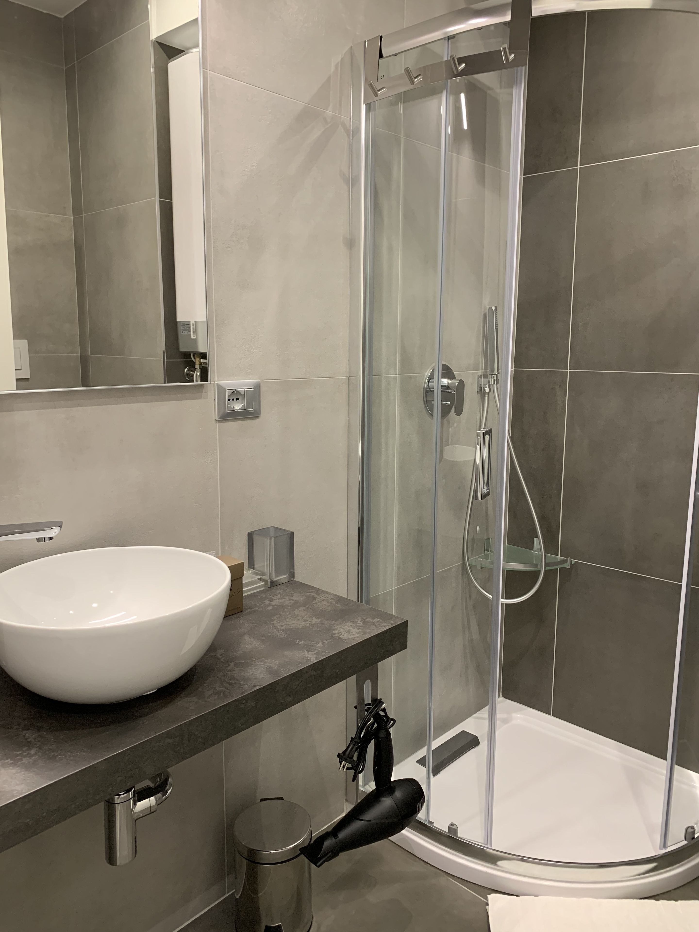 Un baño moderno con un lavabo grande de color blanco, cabina de ducha de vidrio y espejo sobre el lavabo.