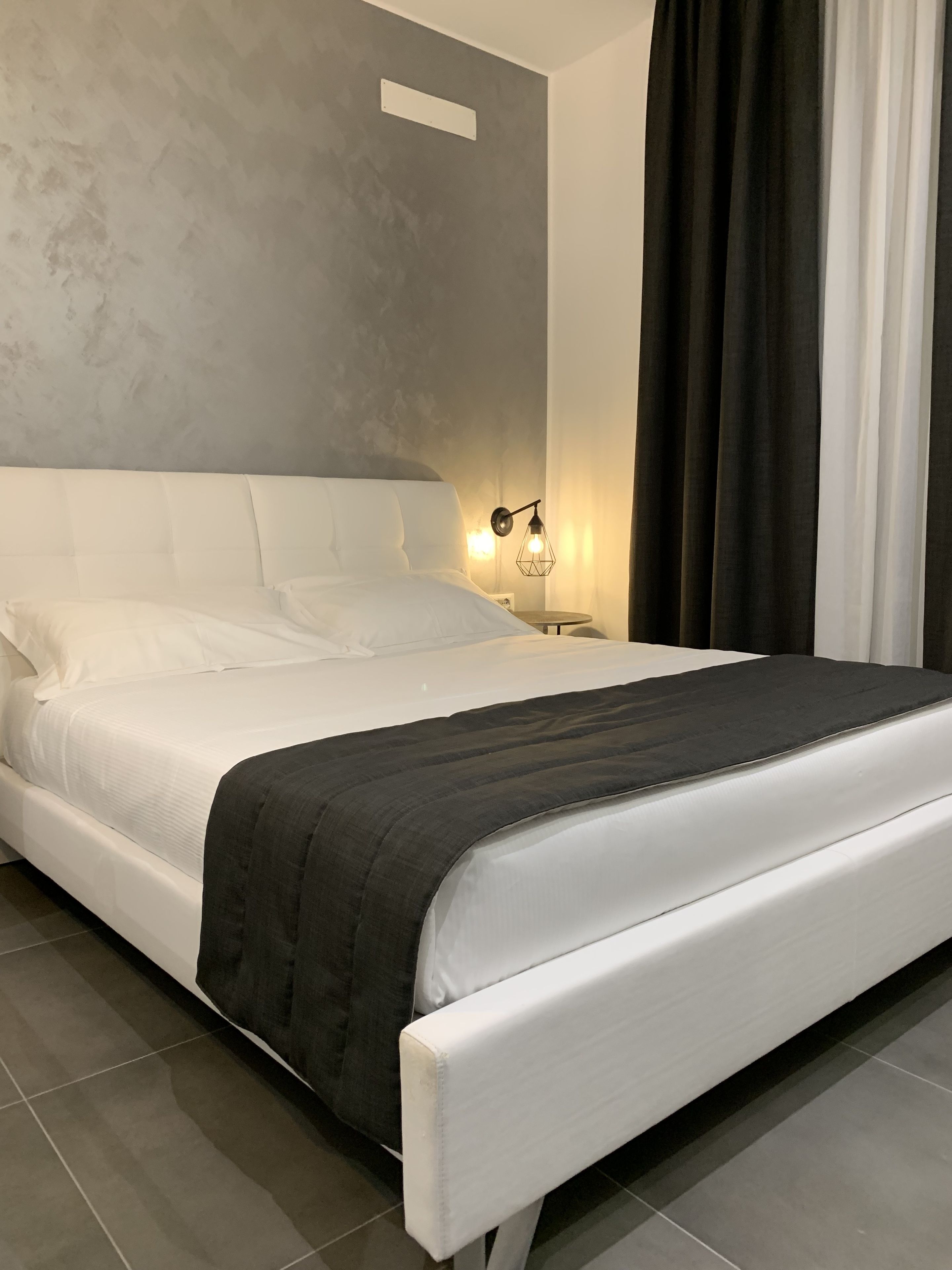 Une chambre à coucher moderne avec un grand lit, une table de chevet avec une lampe et un mur gris à texture.