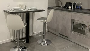 A modern kitchen with a flat-screen TV, two bar stools, a dining table set with plates and glasses, and a built-in oven. - ApartHotel Bossi (Milan)