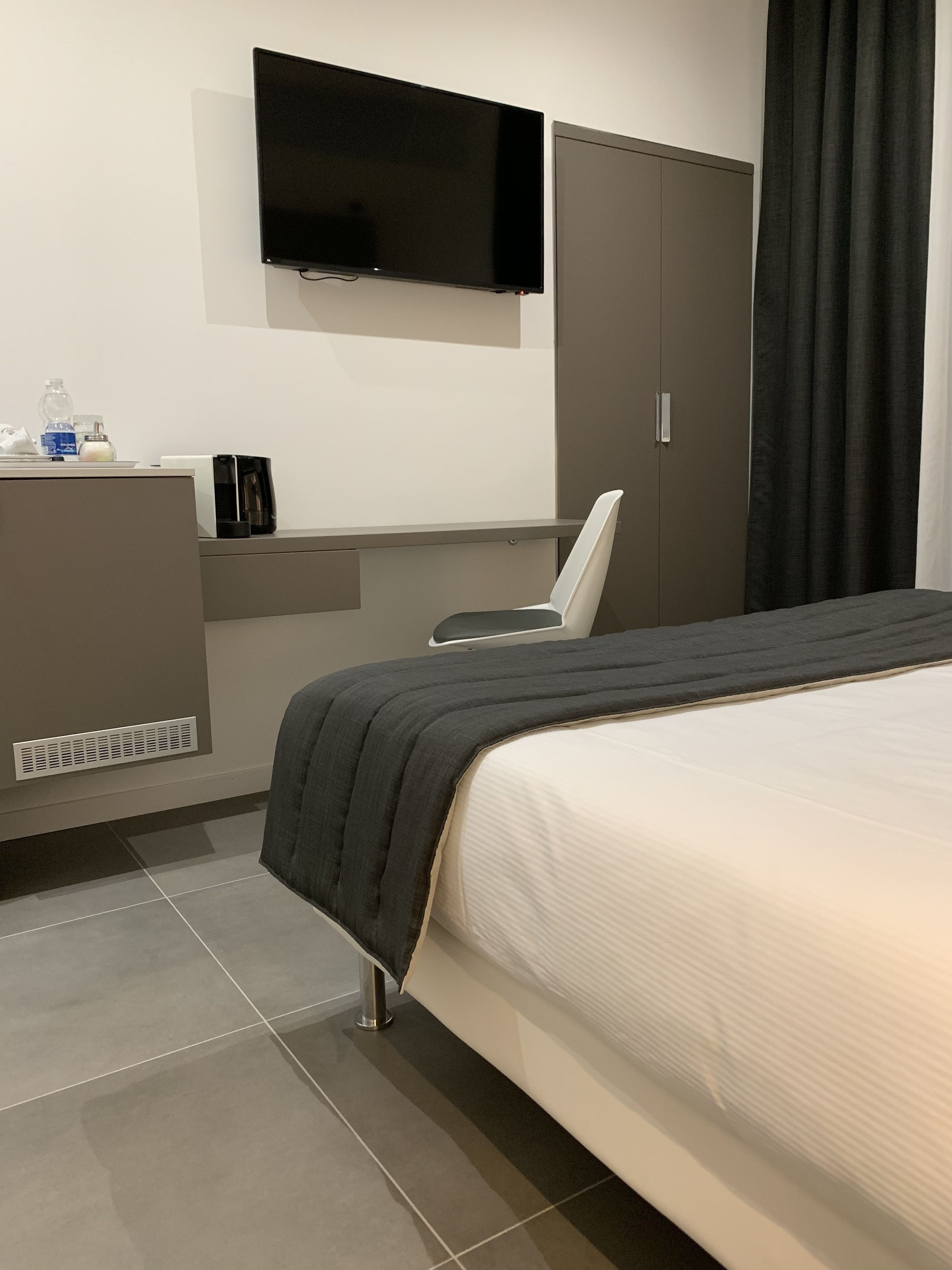 A modern hotel room with a bed, a desk, a chair, a TV, and a wardrobe.