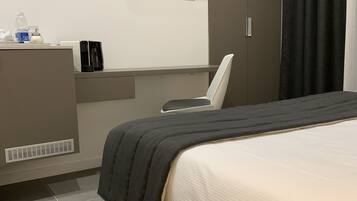 A modern hotel room with a bed, a desk, a chair, a TV, and a wardrobe.