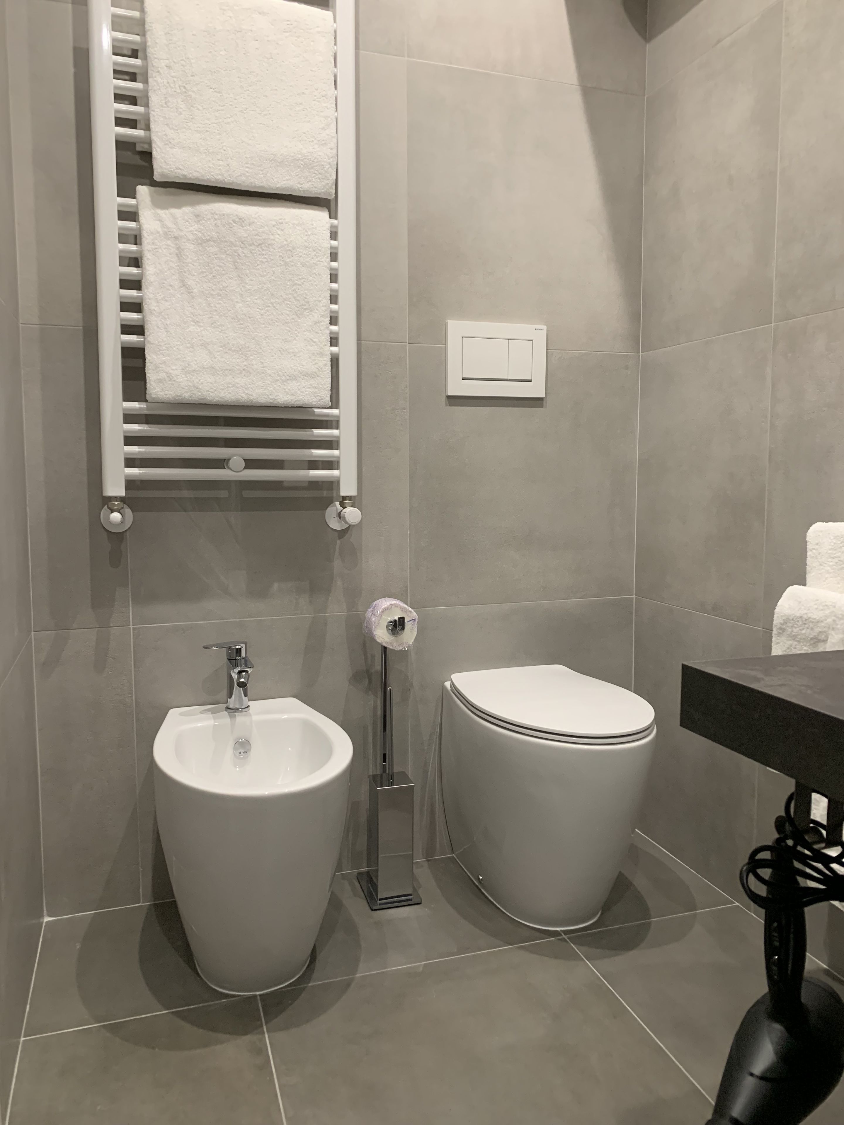 A modern bathroom with a bidet, toilet, towel rack, and a control panel.
