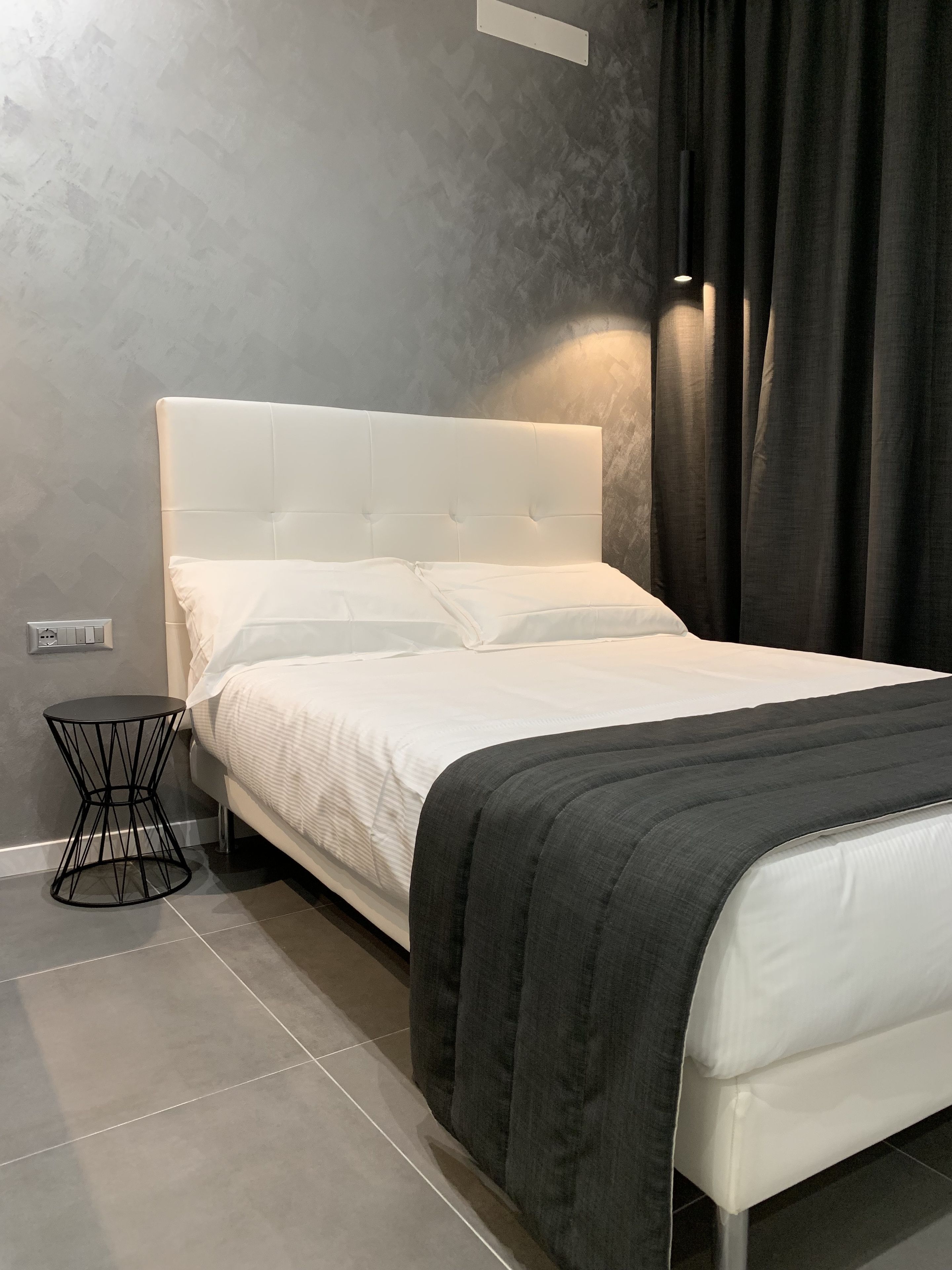 A modern bedroom with a white bed, a black side table, and a grey textured wall.