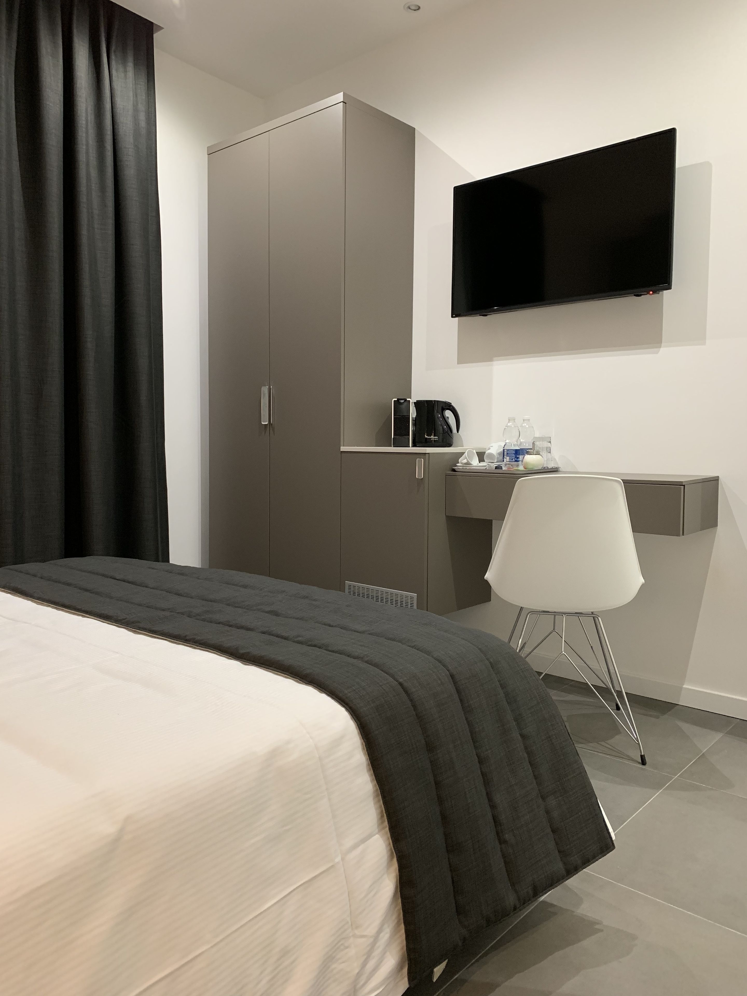 Una habitación de hotel moderna con una cama, un escritorio, una silla, un televisor y un armario.