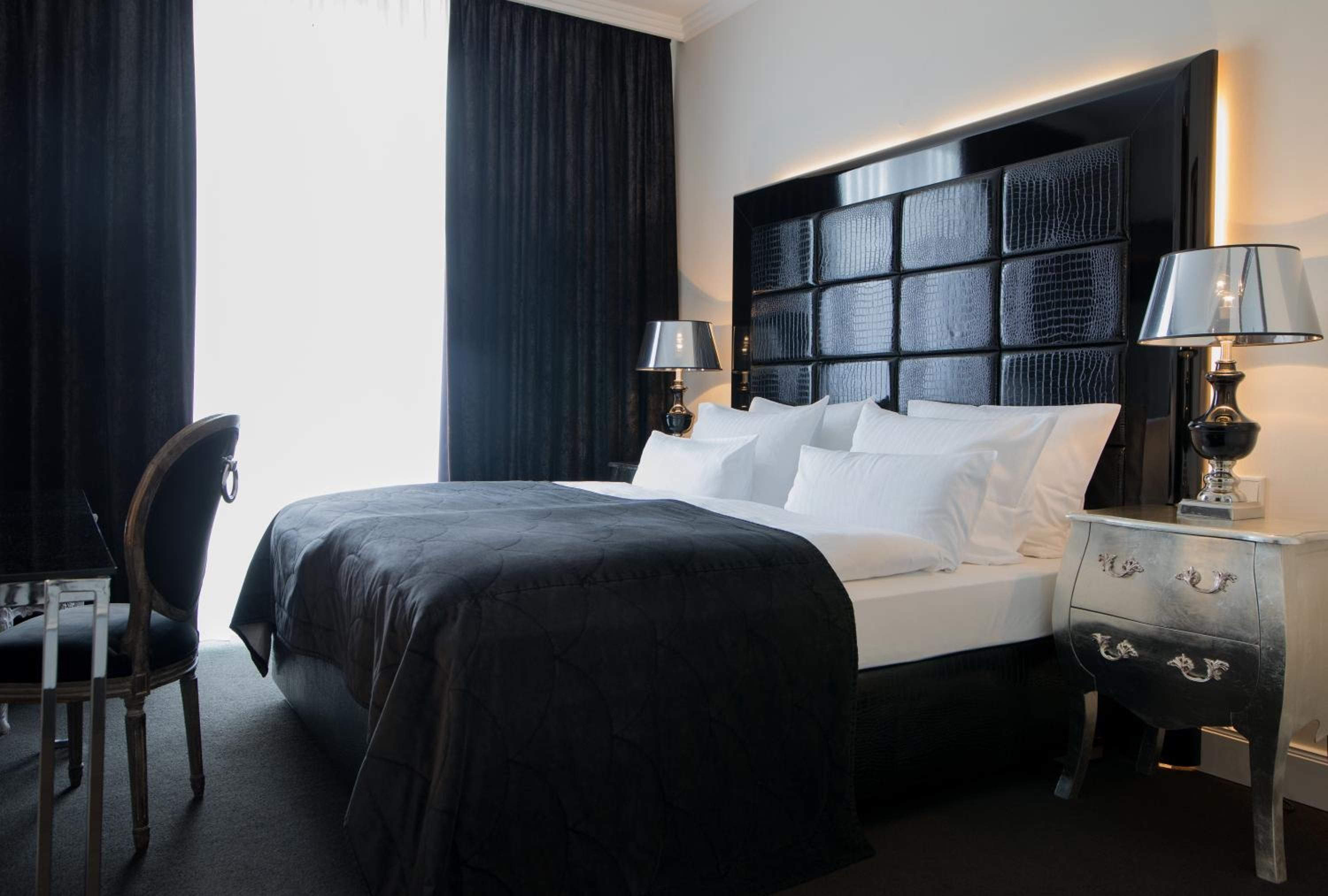 Ein Hotelzimmer mit einem großen Bett, zwei Nachttischen mit Lampen, einem Sessel und Blick ins Freie.
