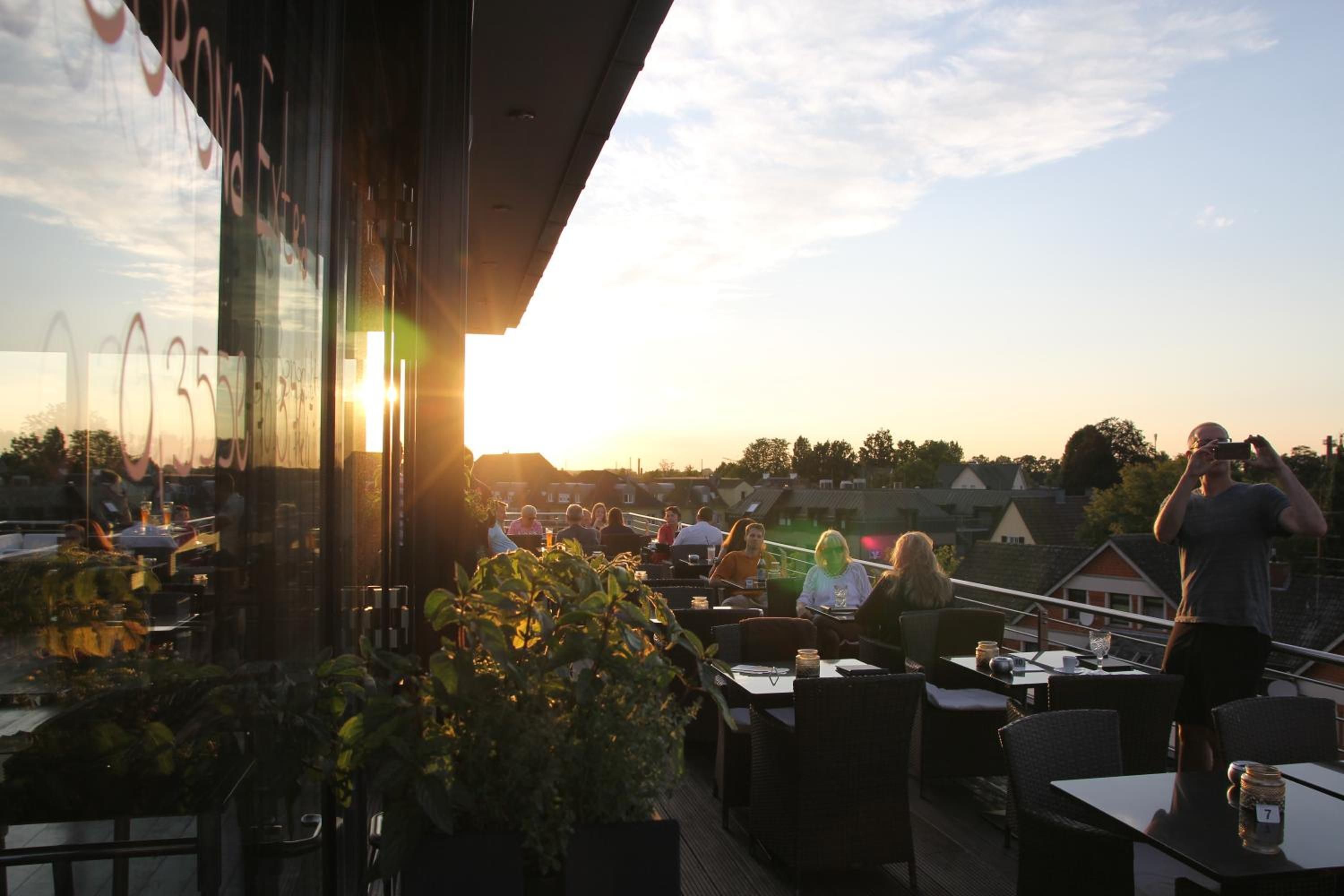 Un área de estar al aire libre con mesas y sillas, con vistas a una zona residencial al atardecer.