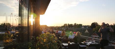 An outdoor seating area with tables and chairs, overlooking a residential area during sunset.