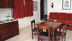 Una cocina con un lavamanos, armarios de madera, una mesa de comedor con sillas, un sofá rojo y un cuadro en la pared.