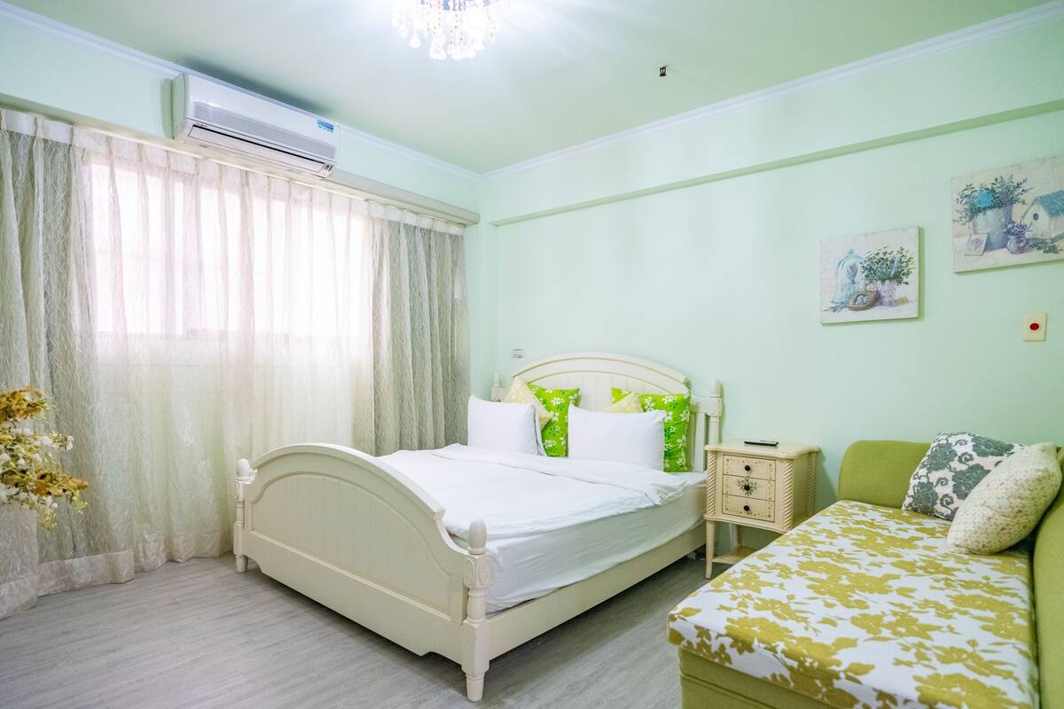 A bedroom with a bed, bedside tables, a nightstand, a sofa, and a window with curtains.