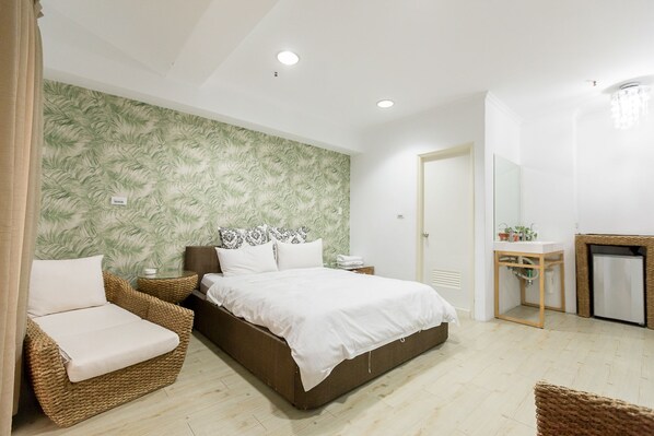 Un dormitorio con una cama, dos sillones de mimbre, una mesita de noche, un espejo, un pequeño lavabo con encimera y una chimenea.