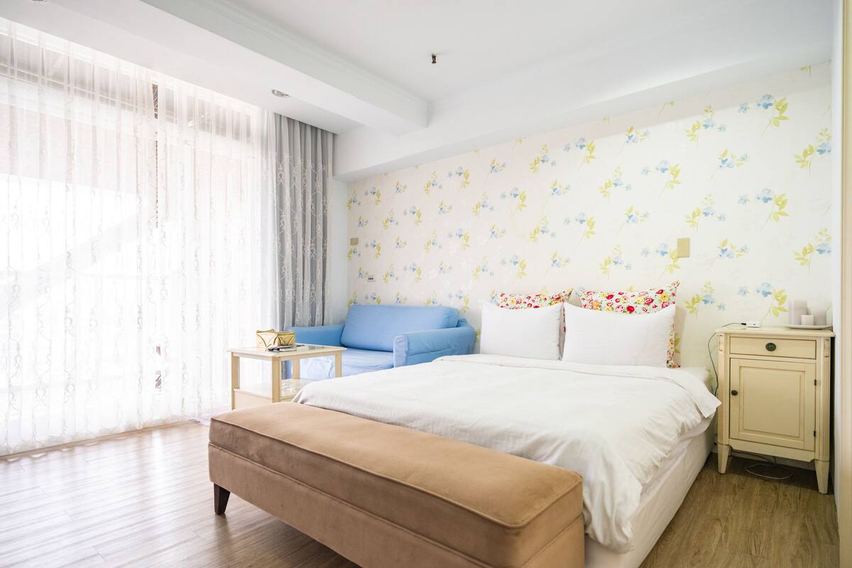 A bedroom with a bed, a blue sofa, a wooden nightstand, and a bench.