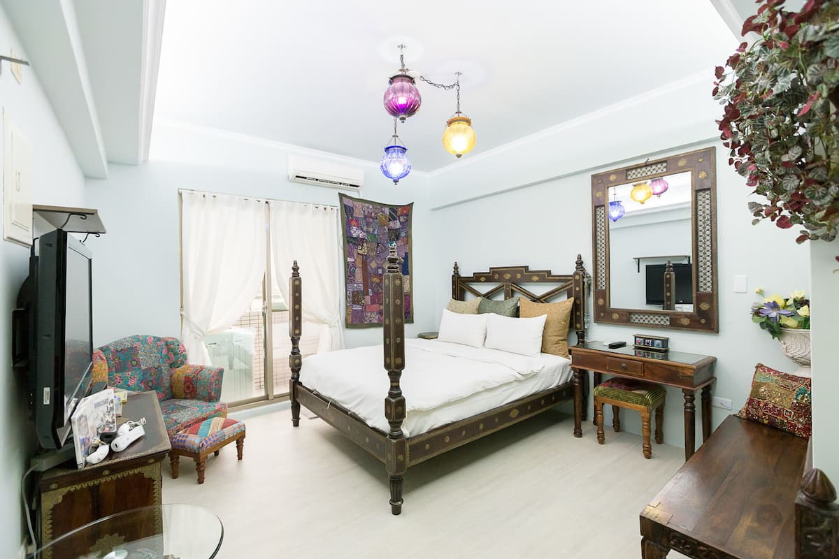 A bedroom with a four-poster bed, a wooden desk, a chair, a television, and a large mirror.