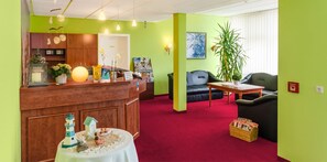A reception area with a wooden desk, a red carpet, a black sofa, and a potted plant. - Hotel Muenkel (Hannover)