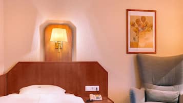 A hotel room with a bed, a bedside lamp, a telephone, a chair, and a painting on the wall.