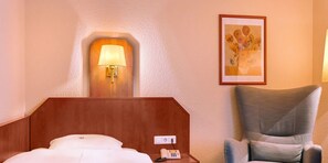 A hotel room with a bed, a bedside lamp, a telephone, a chair, and a painting on the wall. - Hotel Muenkel (Hannover)