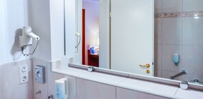 A bathroom with a mirror, a hairdryer, a towel dispenser, and a toilet paper holder. - Hotel Muenkel (Hannover)